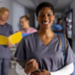 portrait of happy african american female doctor wearing scrubs with tablet in corridor at hospital. hospital, communication, medicine, healthcare and work, unaltered.